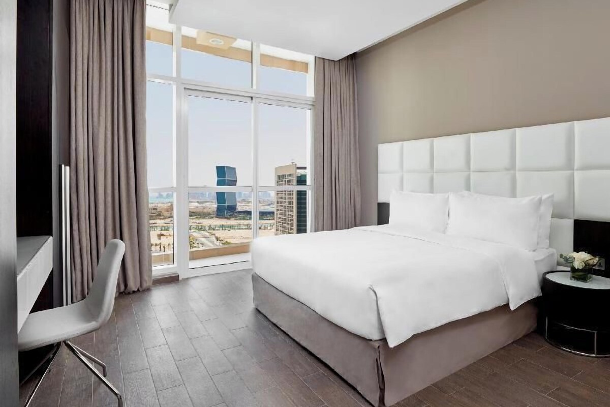 A hotel room with a large bed, a desk, and a view of the cityscape.