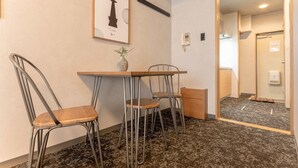 A hotel room with a wooden table and two metal chairs, a framed chess piece on the wall, and a small potted plant. - b&Namba3 (Osaka)