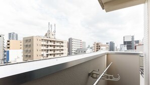A balcony with a metal railing and a hook, overlooking a cityscape with various buildings. - b&Namba3 (Osaka)