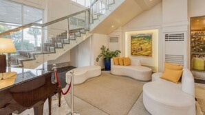 Un amplio salón con una imponente escalera, un piano y un cuadro grande.