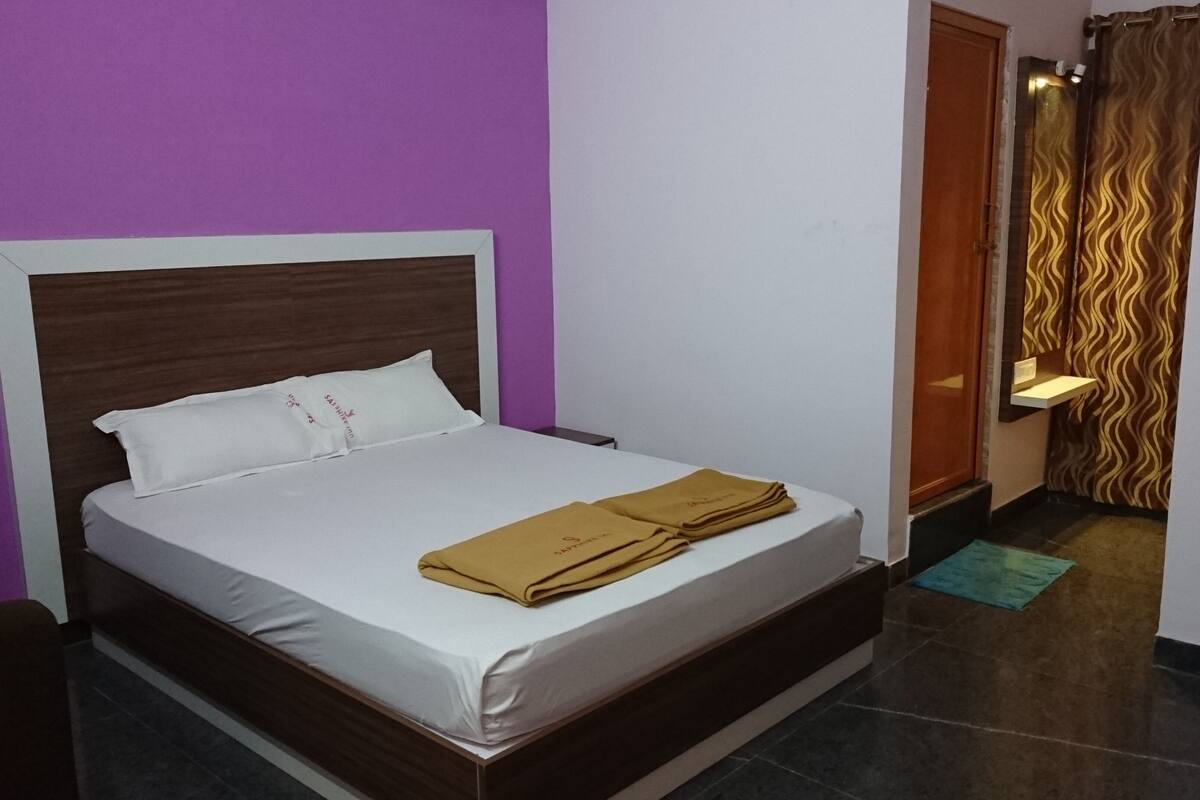 A hotel room with a bed, a wooden headboard, a purple wall, a door, and a patterned curtain.