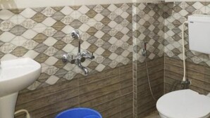 Un baño con lavamanos, inodoro, ducha y un cubo azul.