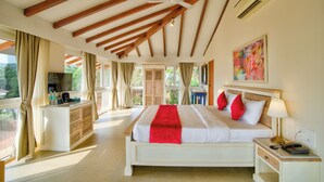 A spacious bedroom with a large bed, a bedside table, a desk, and a ceiling fan. - The Goa Beach Resort Morjim (Morjim)