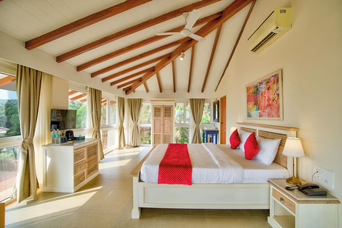 A spacious bedroom with a large bed, a bedside table, a desk, and a ceiling fan.