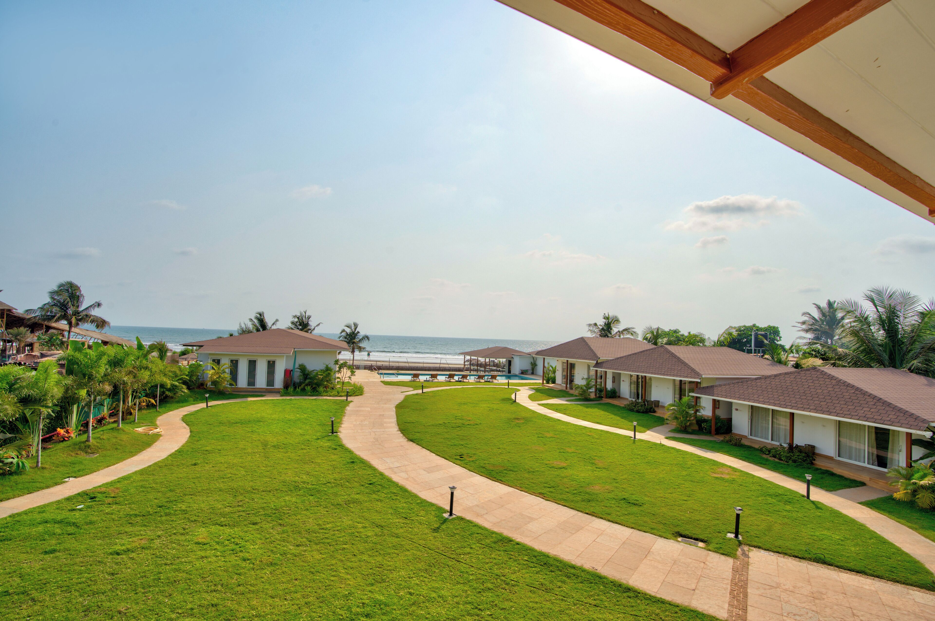 A resort with a pathway leading to a pool area, surrounded by well-maintained lawns and palm trees.