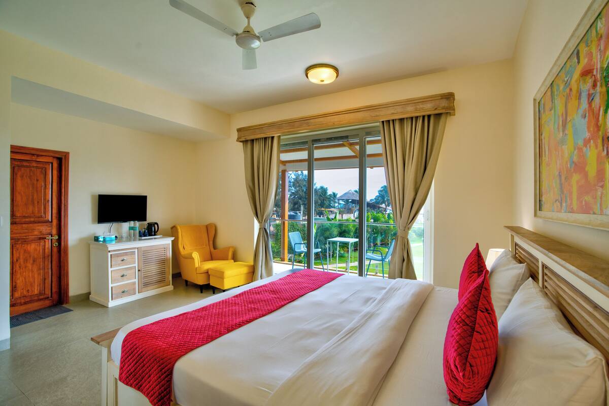 A hotel room with a bed, a television, a desk with a coffee maker, a chair, and a balcony with a view.