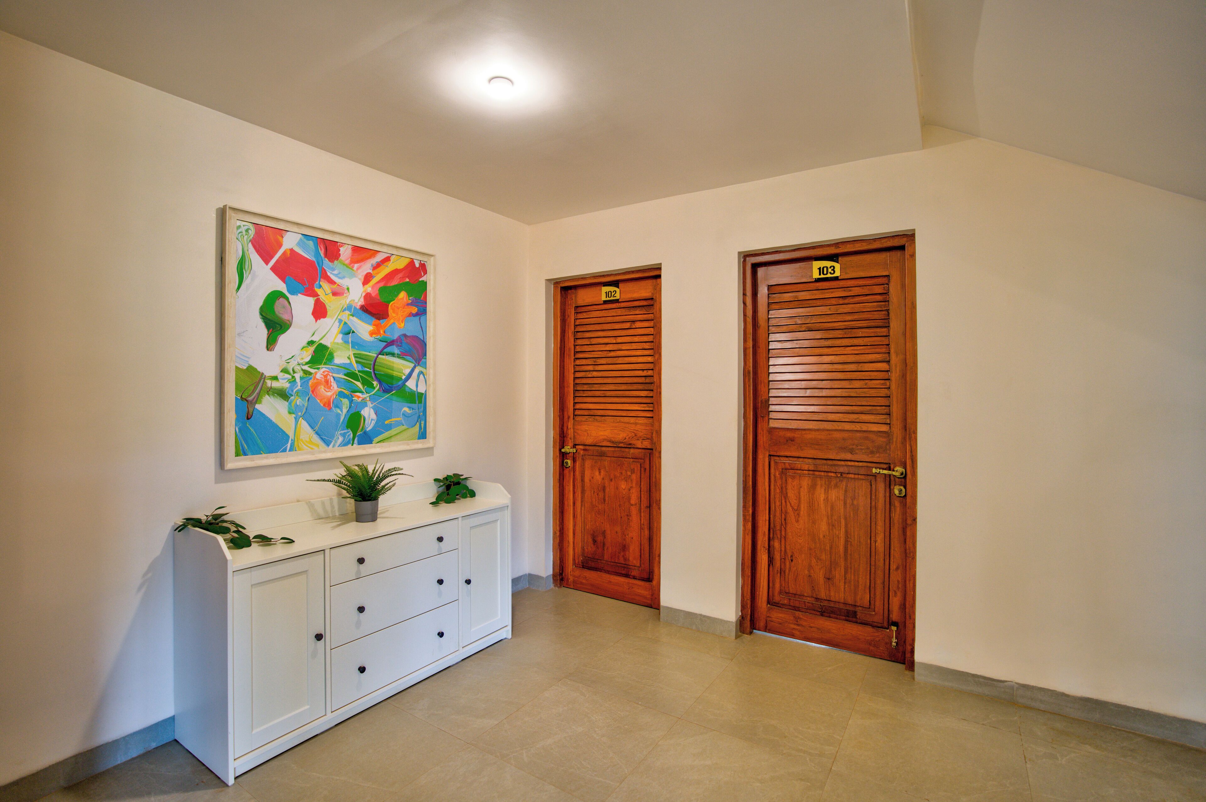A hallway with a white console table, a colorful abstract painting, and two wooden doors labeled 102 and 103.