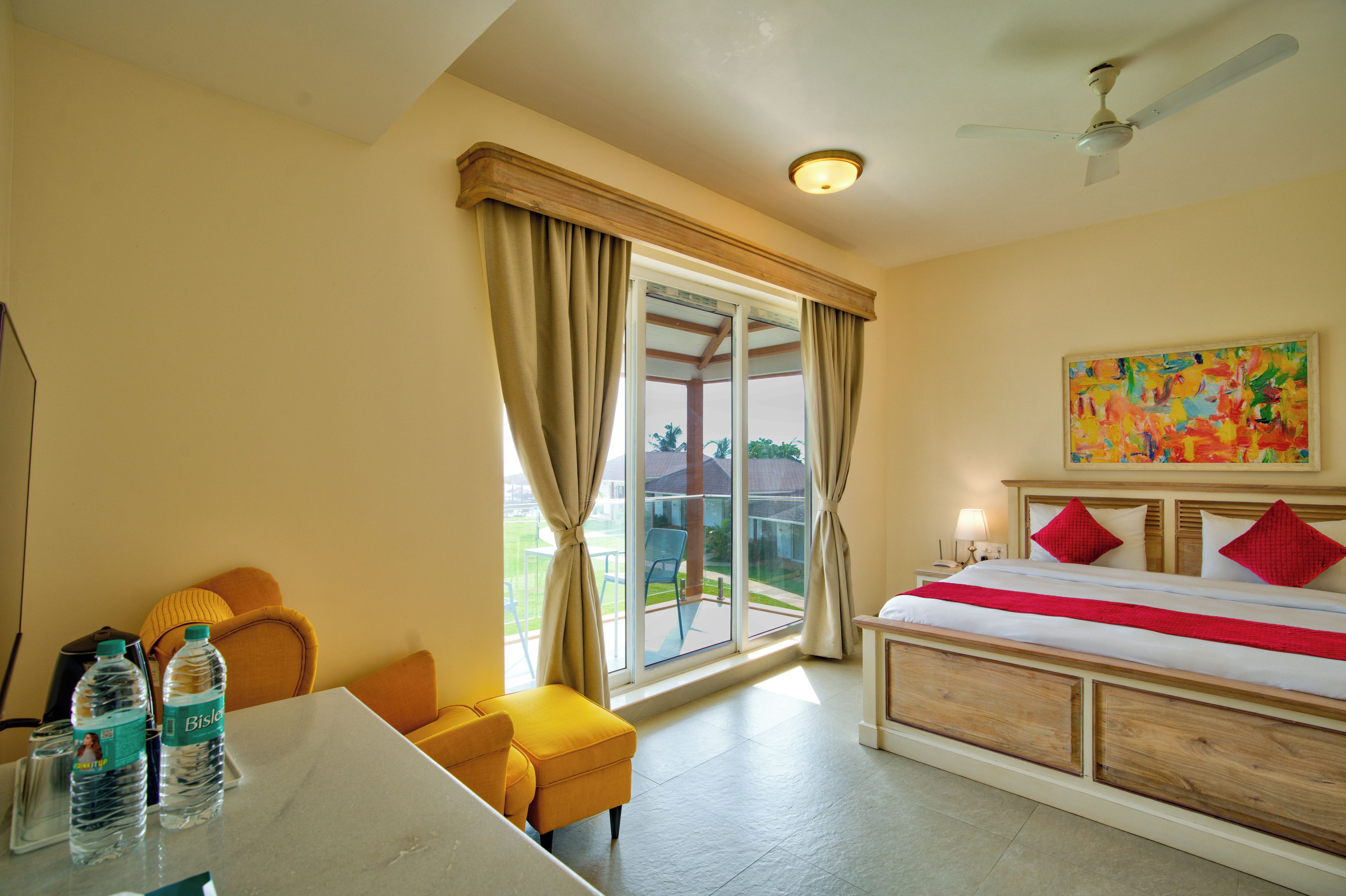 A hotel room with a bed, a desk with water bottles, a chair, and a view of the outdoors.