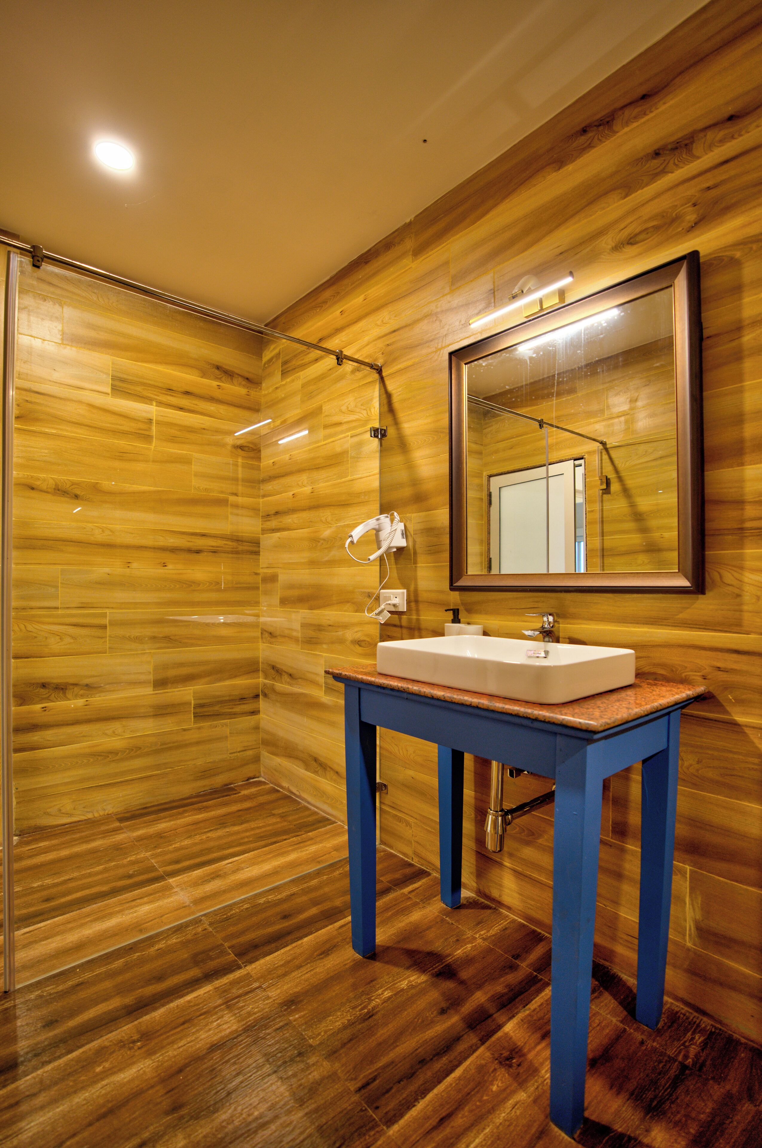 Un baño con paredes de madera, un tocador azul, un lavamanos blanco y un espejo.