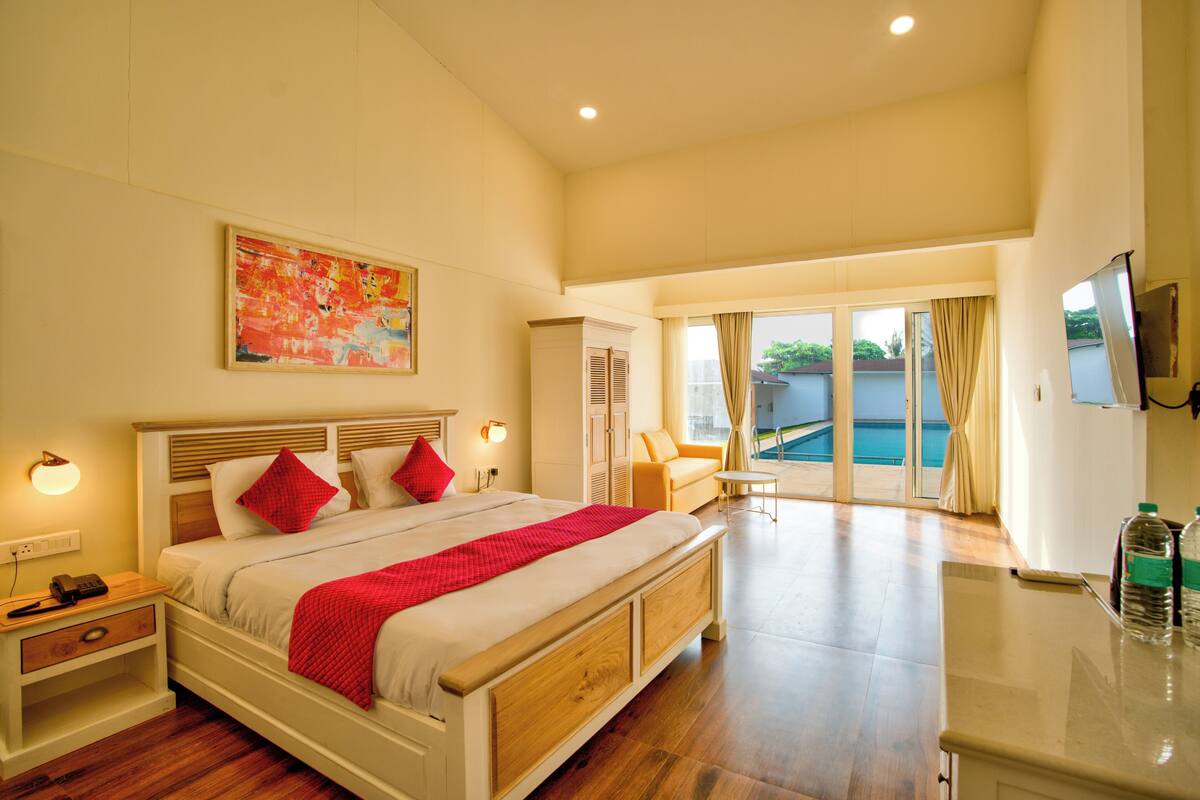 A spacious bedroom with a large bed, a television, and a view of a swimming pool.