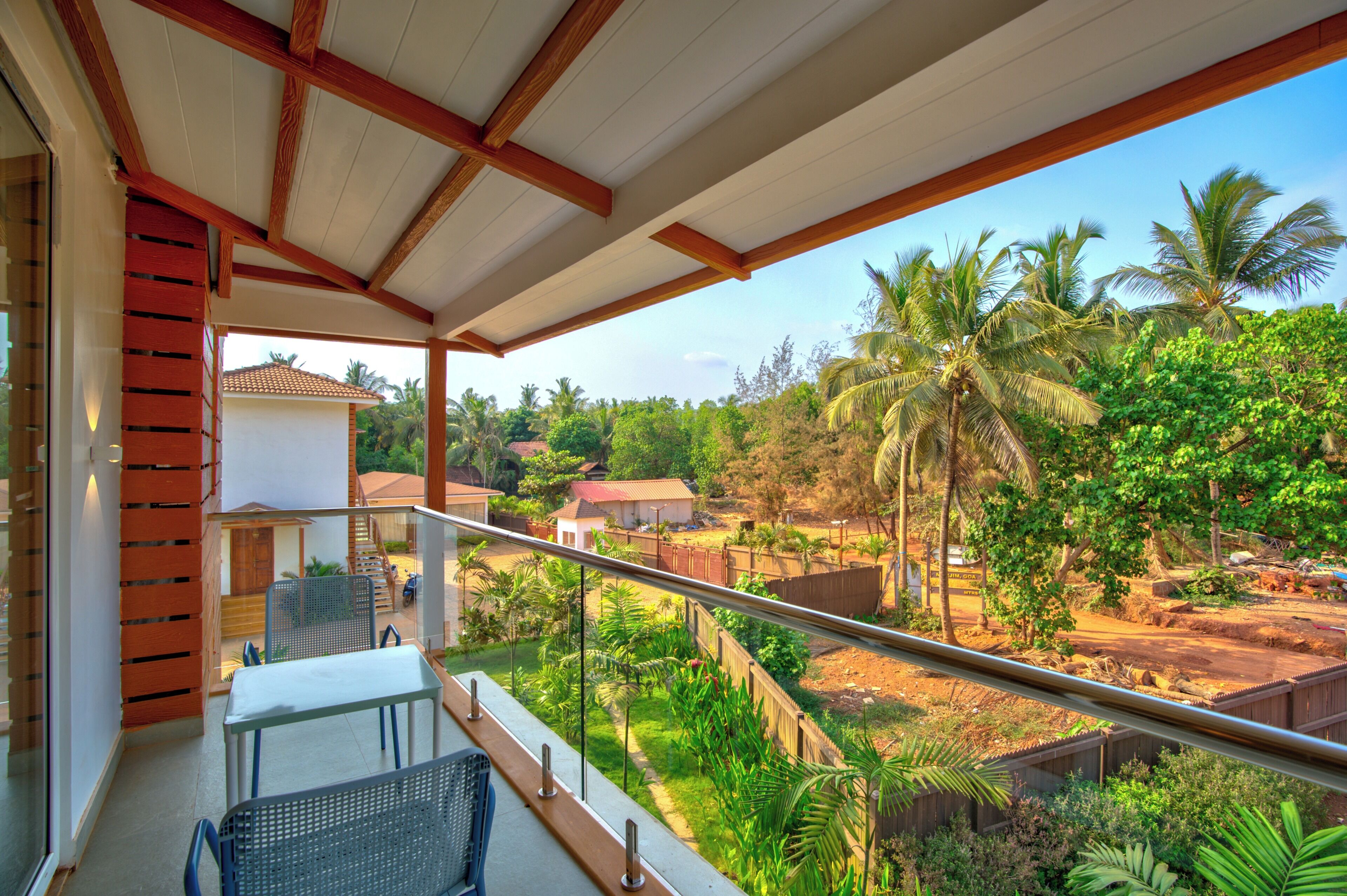 A balcony with a view of a lush garden and a house in the background.