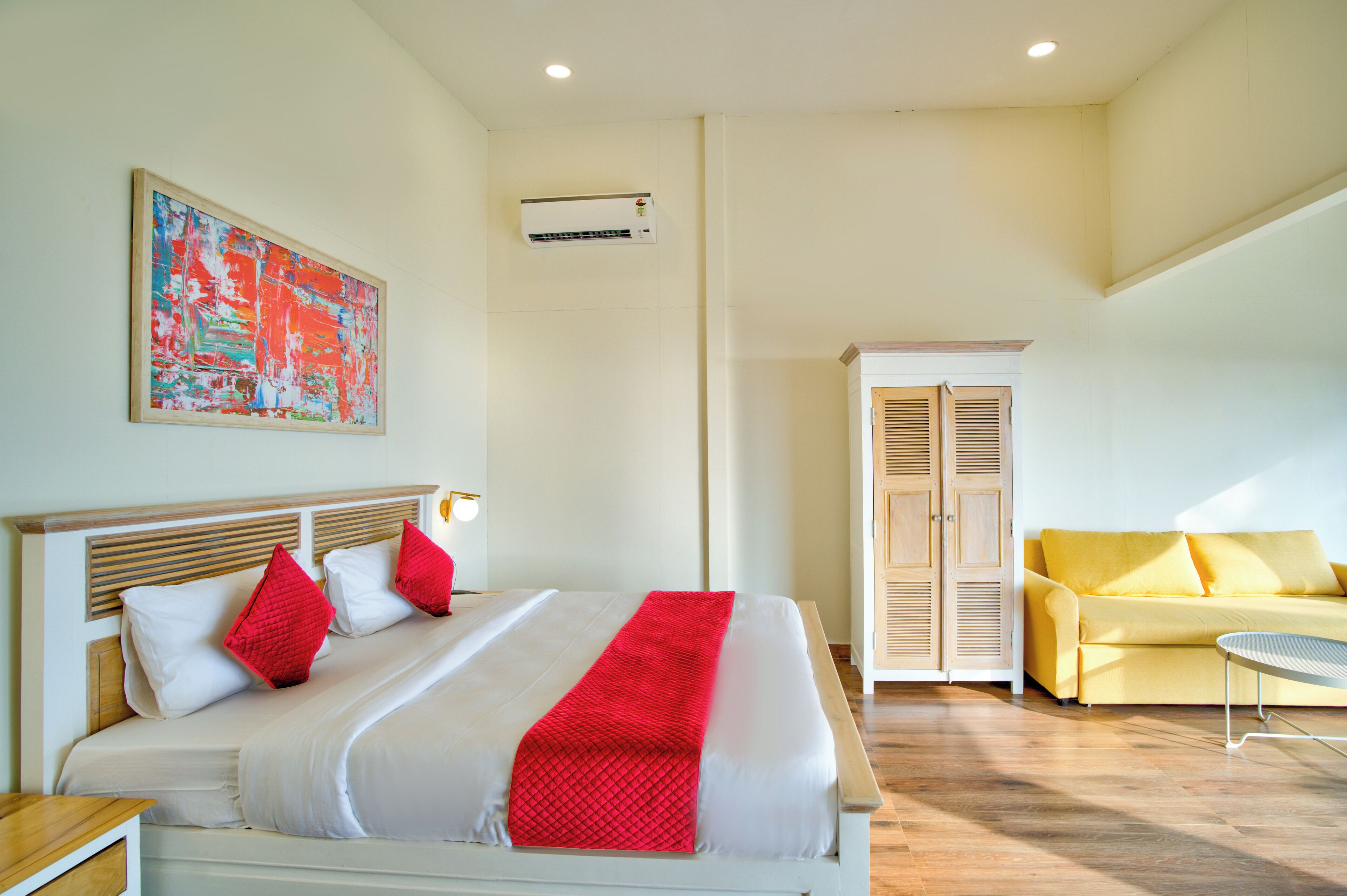 A hotel room with a bed, a yellow sofa, a wardrobe, and a painting on the wall.