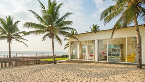 A beachside building with large windows, palm trees, and a sandy beach. - The Goa Beach Resort Morjim (Morjim)