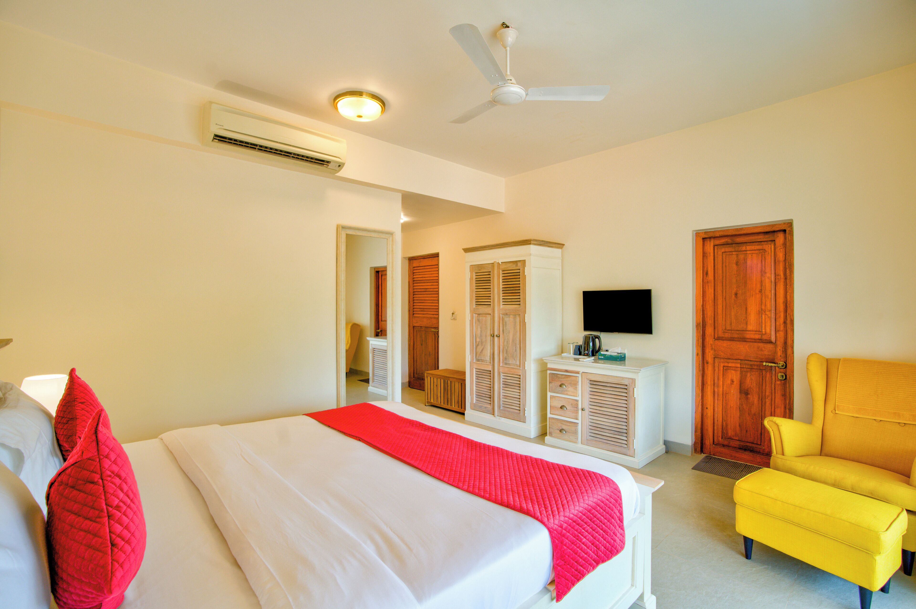 A hotel room with a bed, a yellow armchair, a television, and a wardrobe.