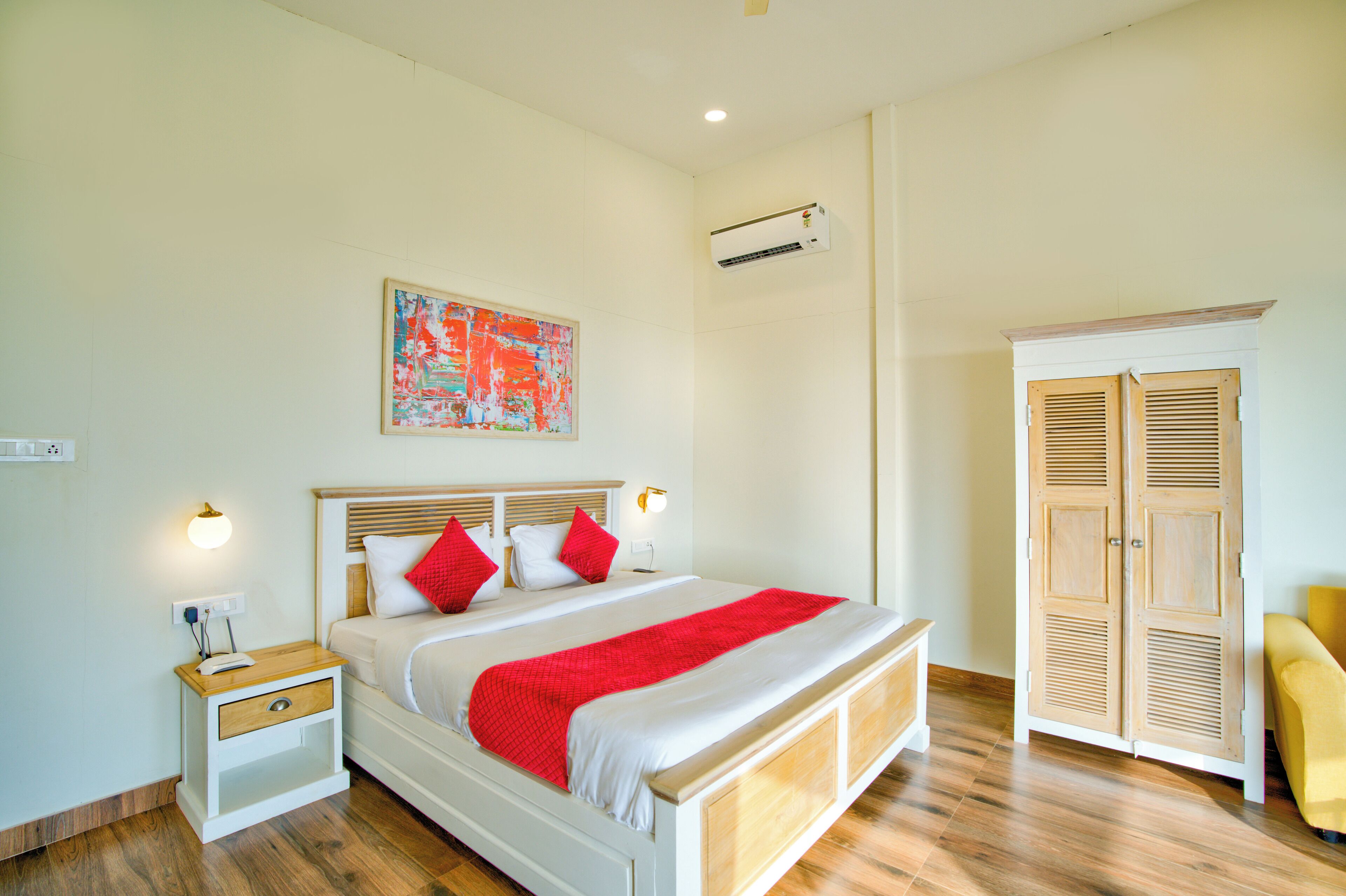A bedroom with a bed, nightstand, wardrobe, and artwork on the wall.