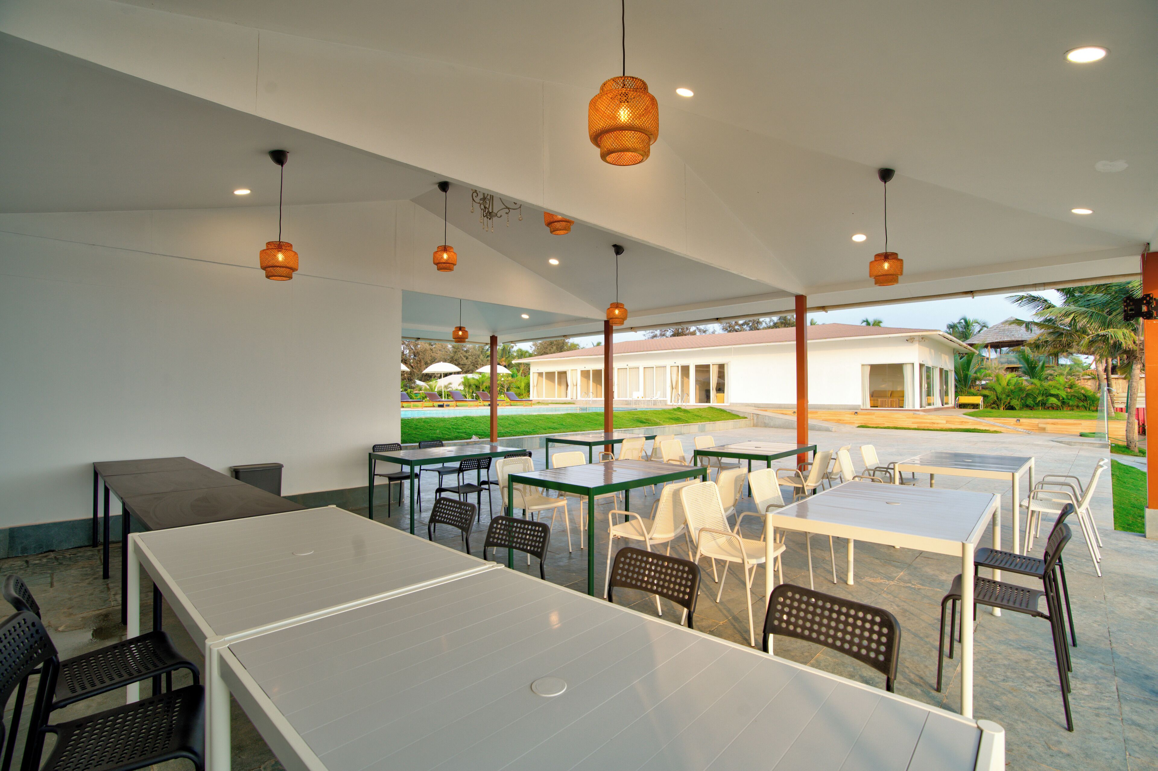 An outdoor dining area with tables and chairs, overhead lighting, and a view of a building in the background.