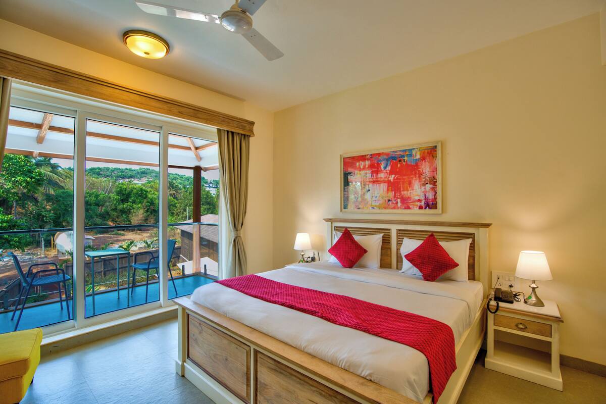 A hotel room with a large bed, two bedside tables, a ceiling fan, and a view of a balcony with outdoor furniture.