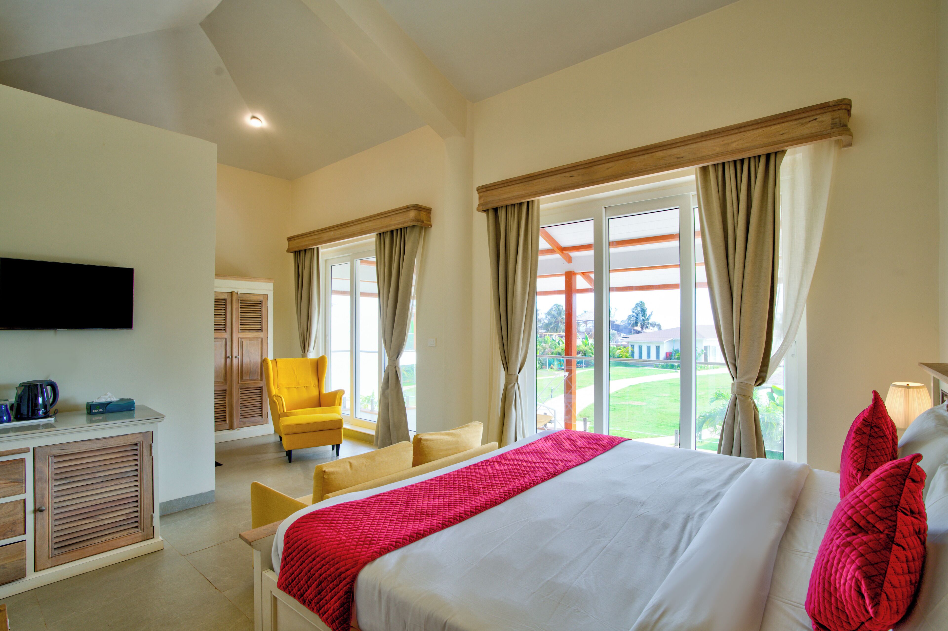 A hotel room with a bed, a TV, a desk, a chair, and large windows with curtains.