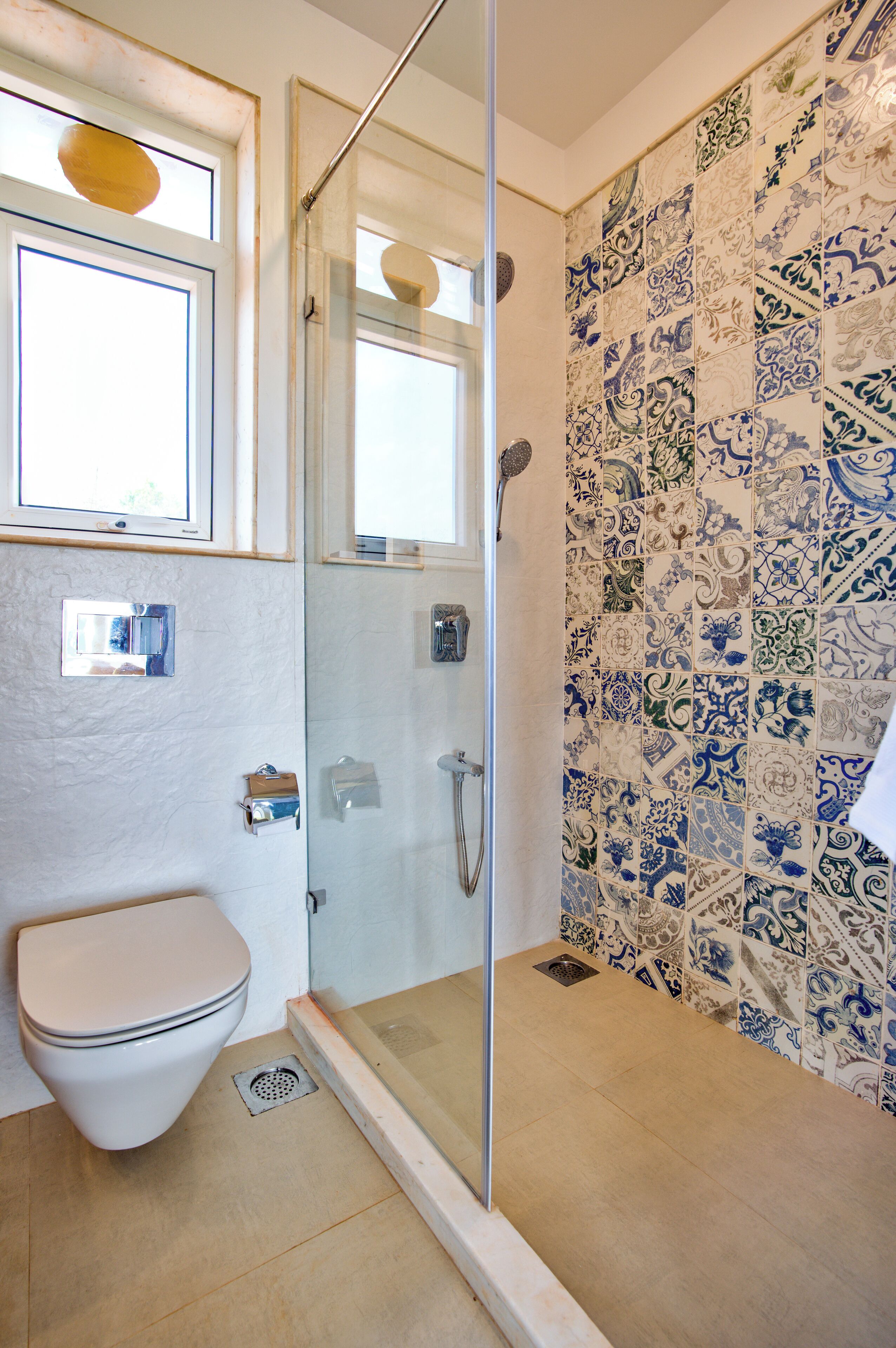 Casa de banho com sanita, chuveiro com porta de vidro e parede revestida a mosaico com padrão azul e branco.