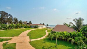 A pathway leading to a building with a tiled roof, surrounded by lush greenery and palm trees. - The Goa Beach Resort Morjim (Morjim)