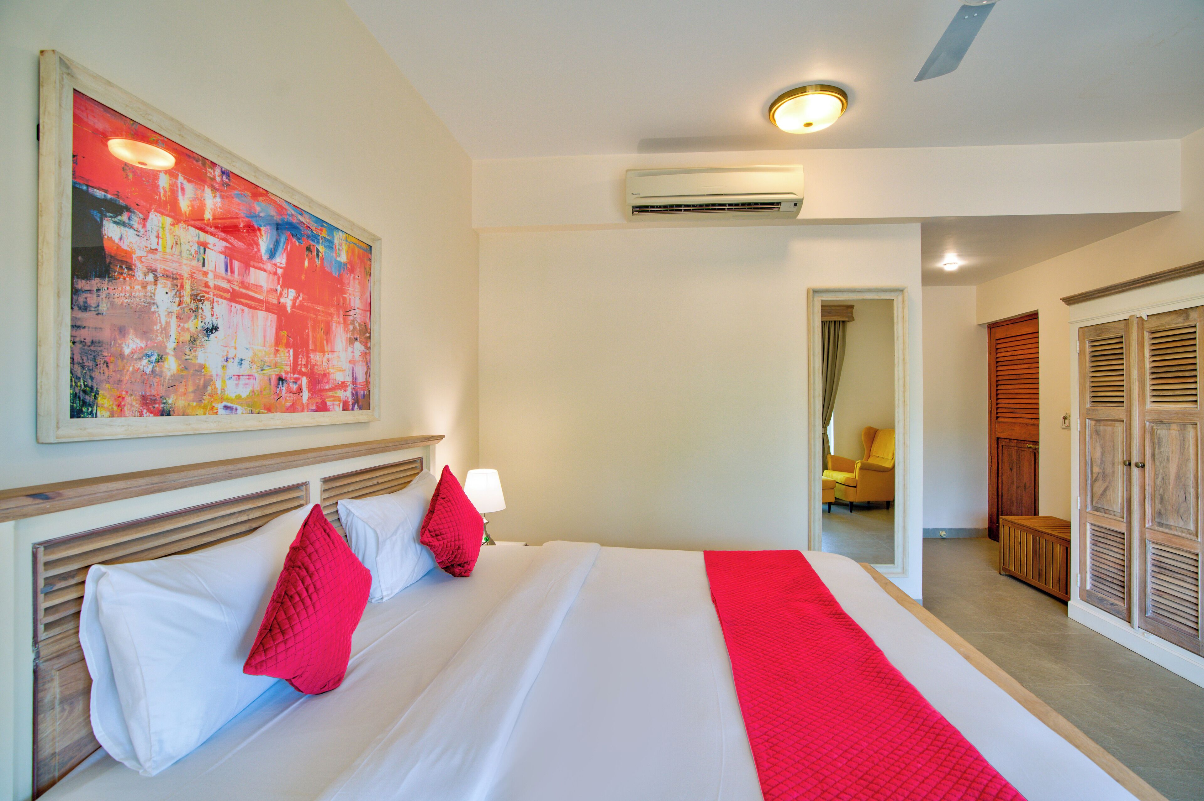 A hotel room with a large bed, a red and white bedspread, a red pillow, a white pillow, a nightstand with a lamp, and a ceiling fan.