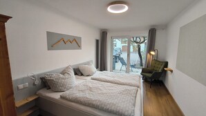 Une chambre d’hôtel avec deux lits, une tête de lit en bois, un luminaire fixé au mur, une vue sur l’extérieur à travers une porte vitrée et un fauteuil vert.