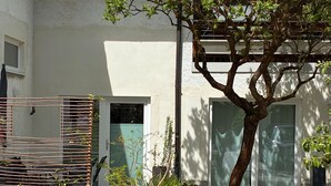 Une cour avec un arbre, des plantes en pot et une clôture en métal.