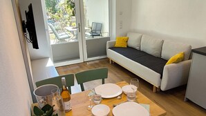 Un coin repas avec une table en bois dressée pour quatre personnes, un luminaire suspendu jaune et un canapé agrémenté de coussins jaunes.