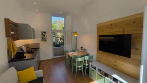 Un espace de vie compact comprenant un coin repas, une kitchenette et un téléviseur à écran plat fixé à un mur en bois.