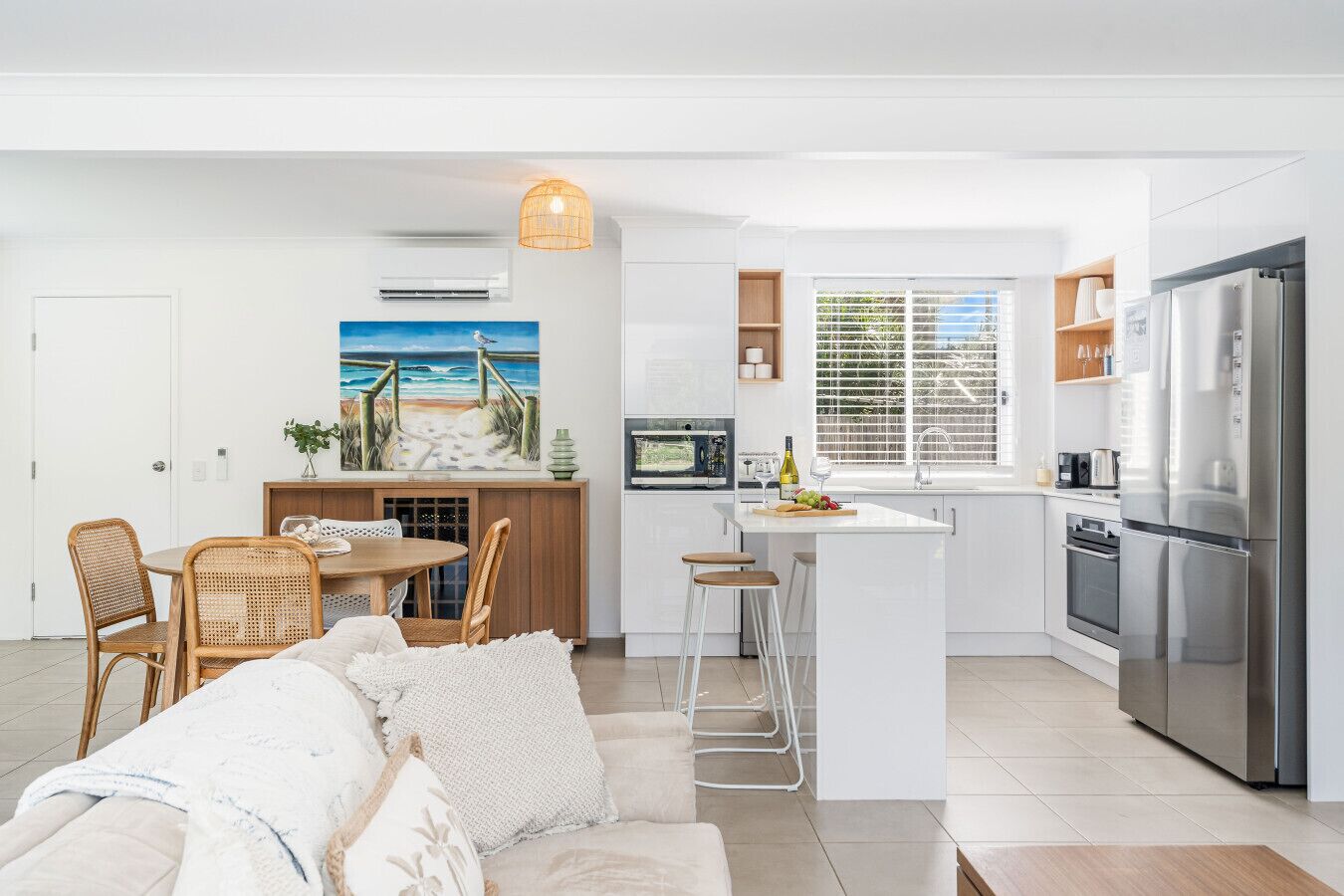 A modern kitchen with a central island, stainless steel appliances, and a dining area with wicker chairs.