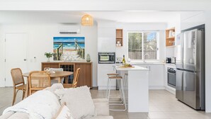Et moderne køkken med en central ø, rustfrie hårde hvidevarer og et spiseområde med fletstole.