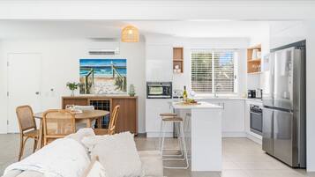 A modern kitchen with a central island, stainless steel appliances, and a dining area with wicker chairs.