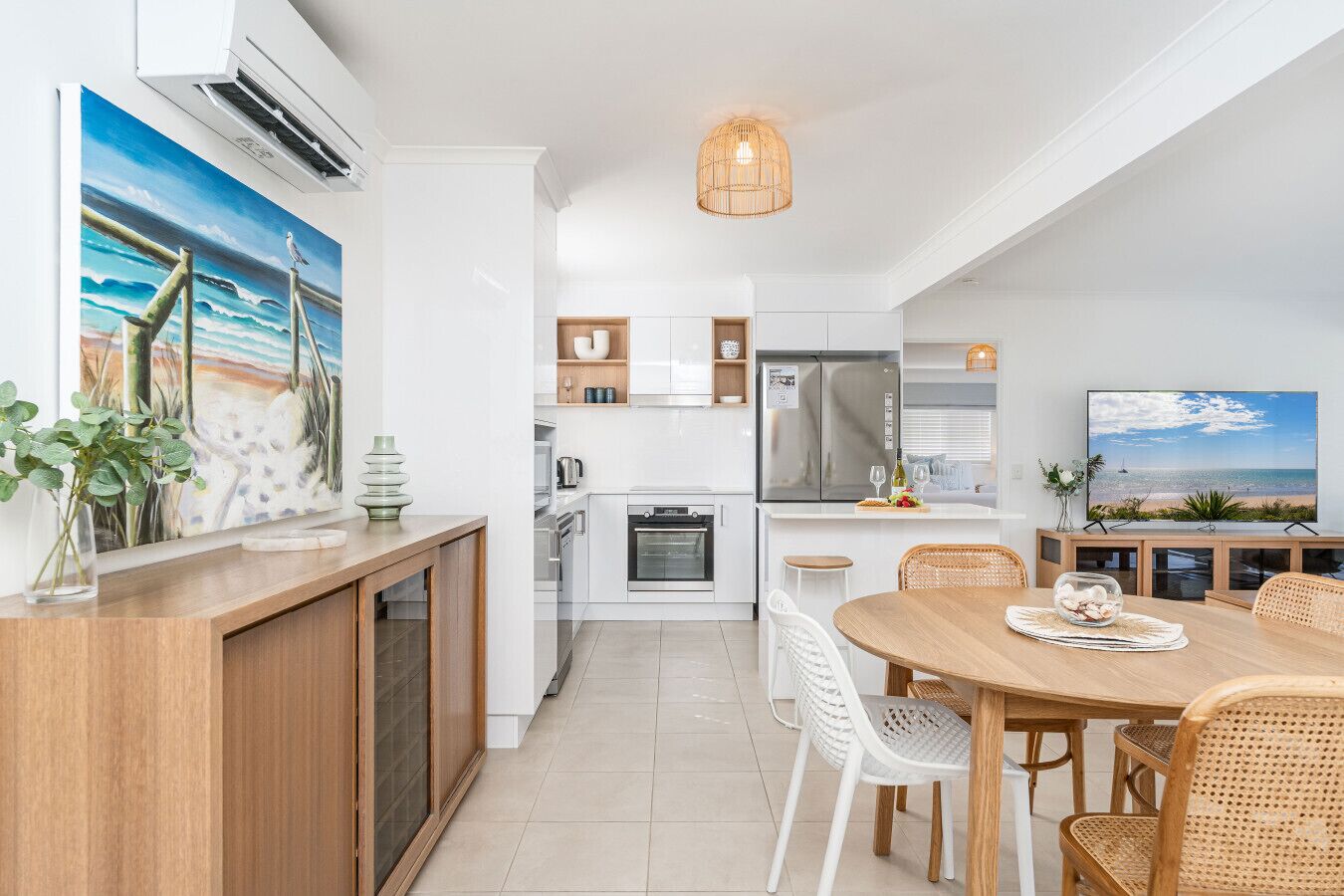 A modern kitchen with white cabinets, a stainless steel refrigerator, and a dining area with a wooden table and wicker chairs.