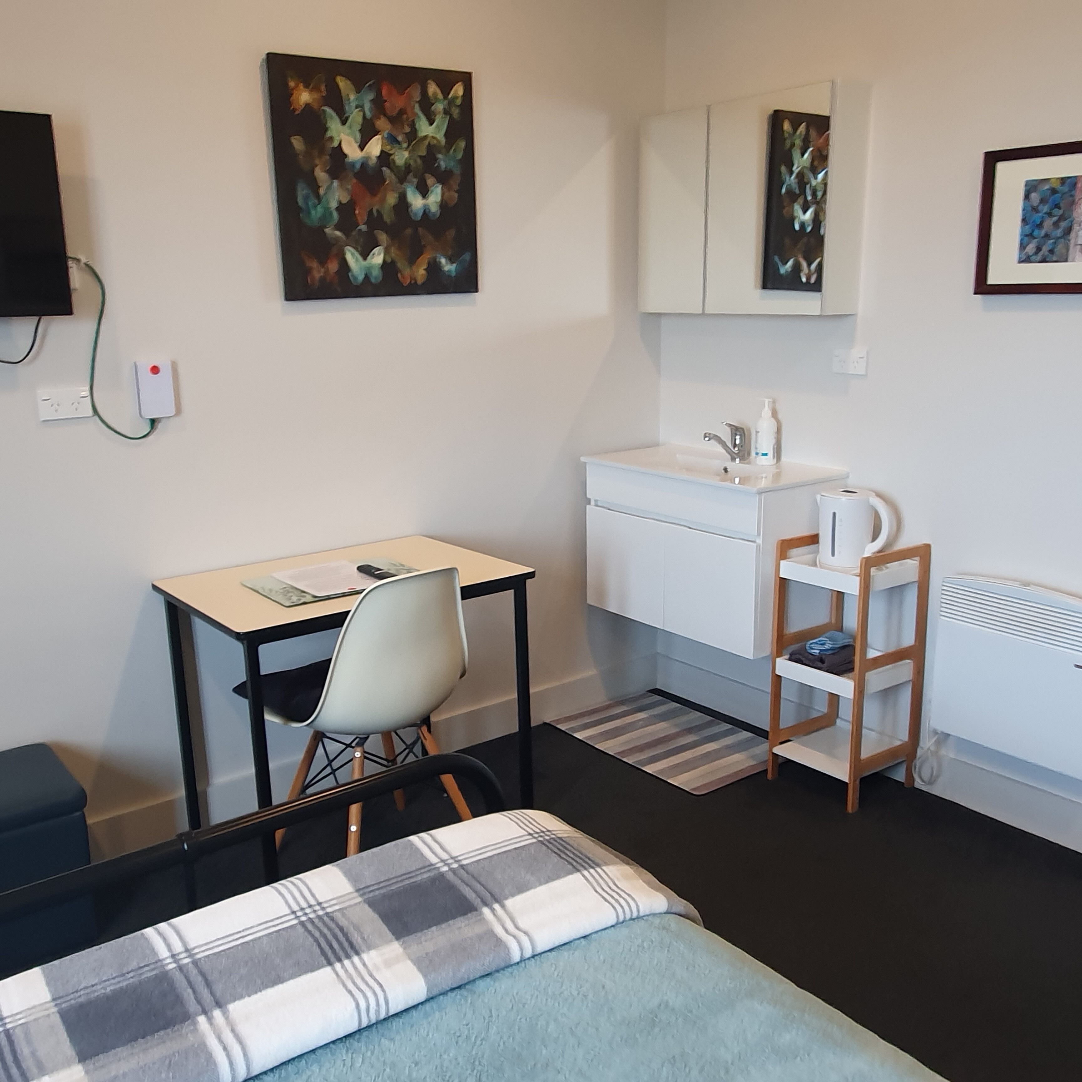 Habitació petita i moderna amb llit, escriptori, cadira, vàter blanc i radiador.