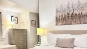 Hotellihuone, jossa on suuri sänky, yöpöytä lampun kanssa, lipasto ja taulu seinällä.
