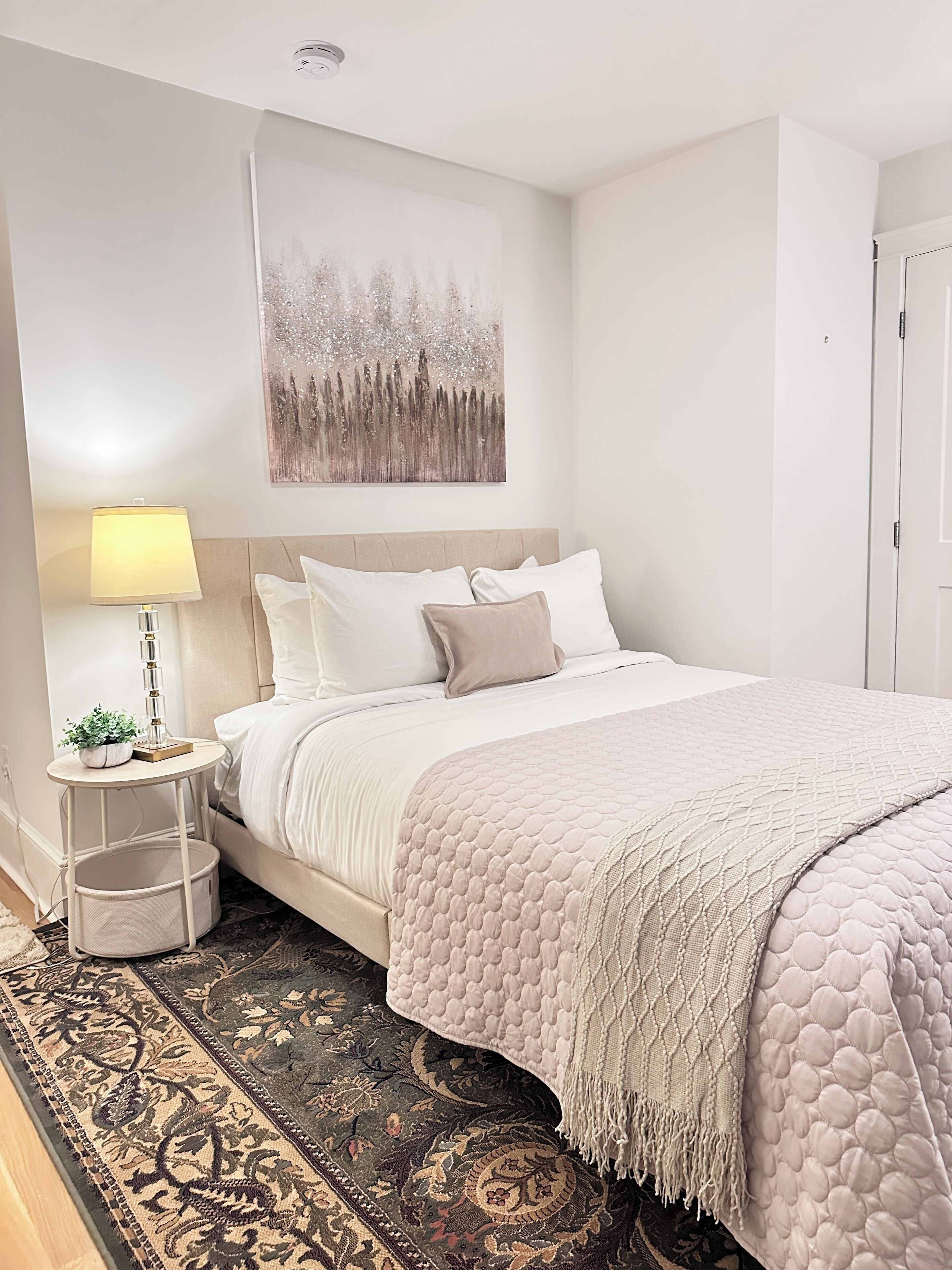 A neatly arranged bedroom with a bed, bedside table, lamp, and a decorative painting on the wall.