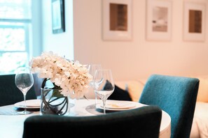 Une table à manger ornée d’un vase de fleurs blanches, de deux verres à vin et d’assiettes.