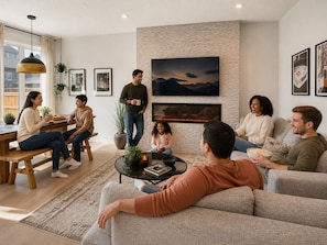 A modern living room with a fireplace, a dining area with a wooden table, and a seating area with sofas and a coffee table. - 7 BR Luxury Home » Central AC » 100` Projector (Calgary)