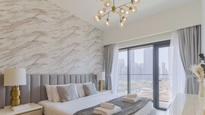Habitación de hotel moderna con pared de mármol, una cama grande con cabecera gris, vistas de la ciudad a través de amplios ventanales y un candelabro.