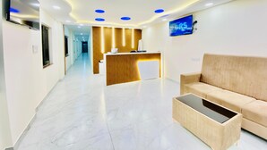 A modern reception area with a wooden reception desk, a beige sofa, and a flat-screen TV on the wall. - Hotel Sahara Tree (Bengaluru)