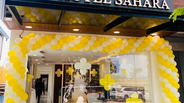 A hotel entrance with a sign in a local language and English, a palm tree logo, and yellow and white balloons. - Hotel Sahara Tree (Bengaluru)