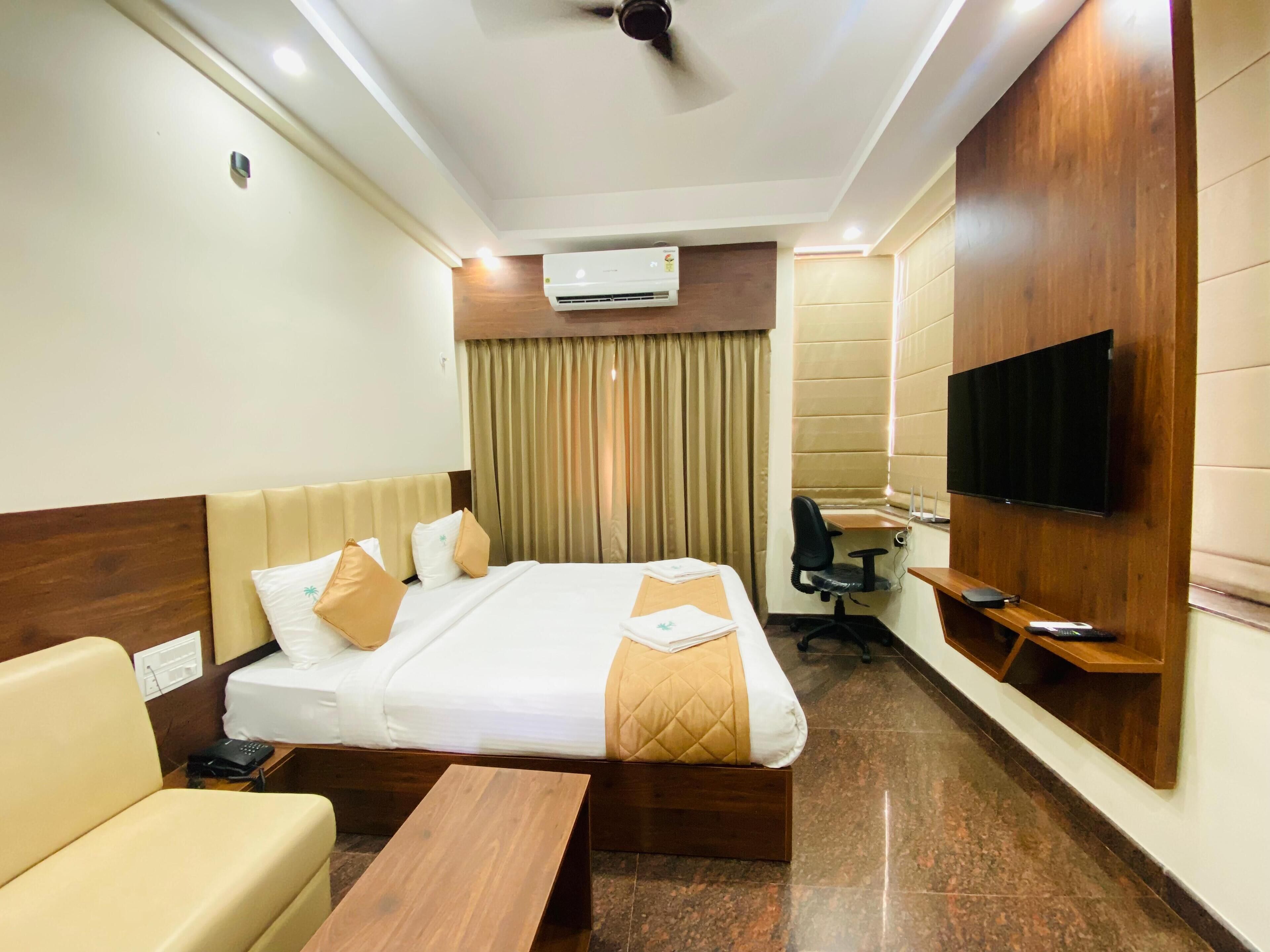 A hotel room with a bed, a desk, a chair, a TV, and an air conditioning unit.