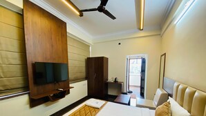 A hotel room with a bed, a TV mounted on the wall, a wardrobe, a desk with a chair, and a ceiling fan. - Hotel Sahara Tree (Bengaluru)