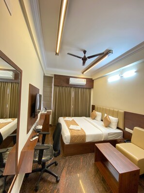 A hotel room with a large bed, a desk, a chair, a mirror, an air conditioning unit, and a ceiling fan. - Hotel Sahara Tree (Bengaluru)