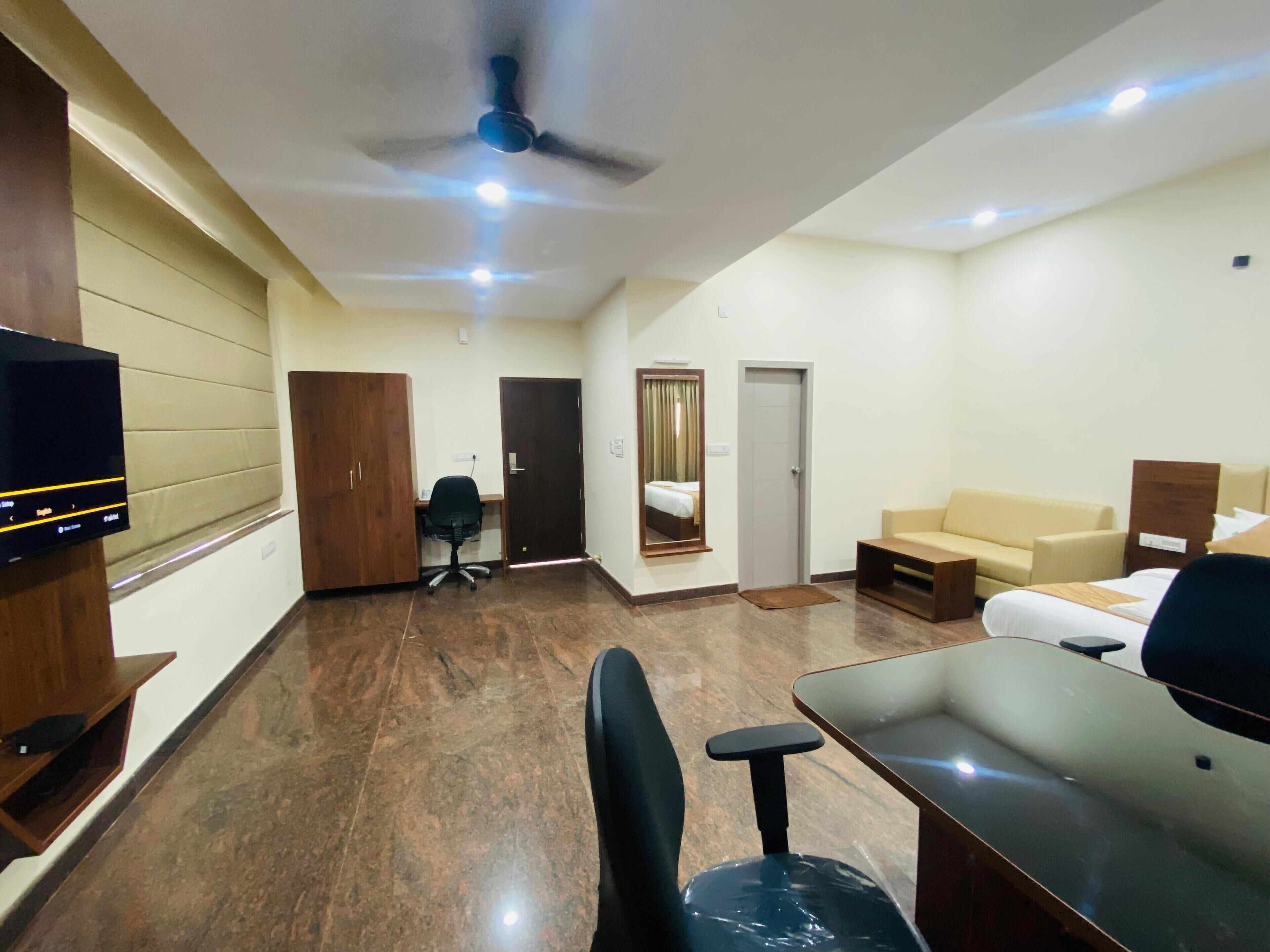 Habitación de hotel con una cama, un escritorio, una silla, un televisor, un ventilador de techo y una puerta.
