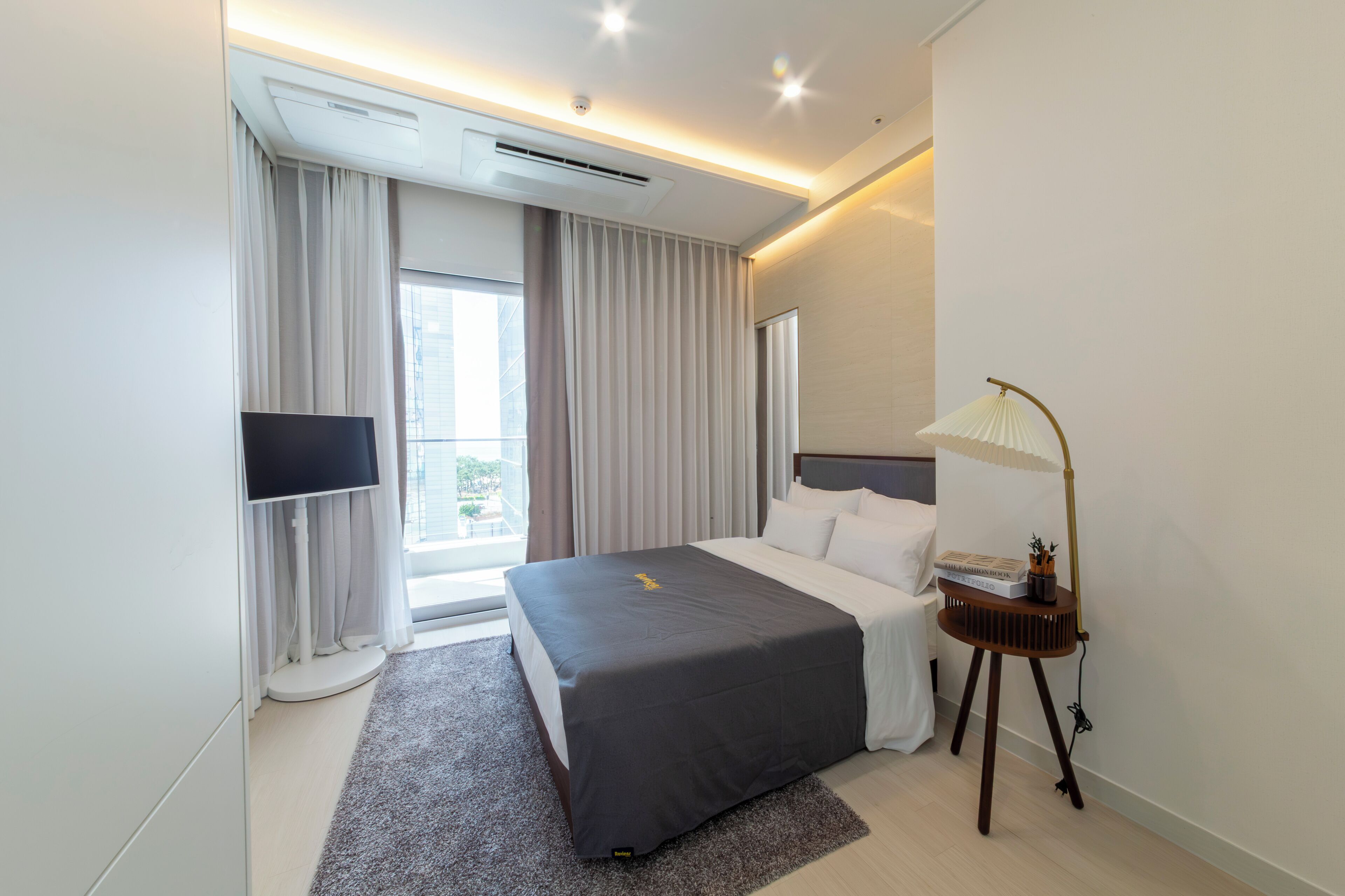 Une chambre d’hôtel moderne dotée d’un grand lit, d’un téléviseur à écran plat, d’une table de chevet avec une lampe et offrant une vue sur l’extérieur.