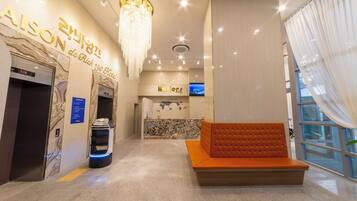 A hotel lobby with a reception desk, a seating area, and a self-service kiosk.