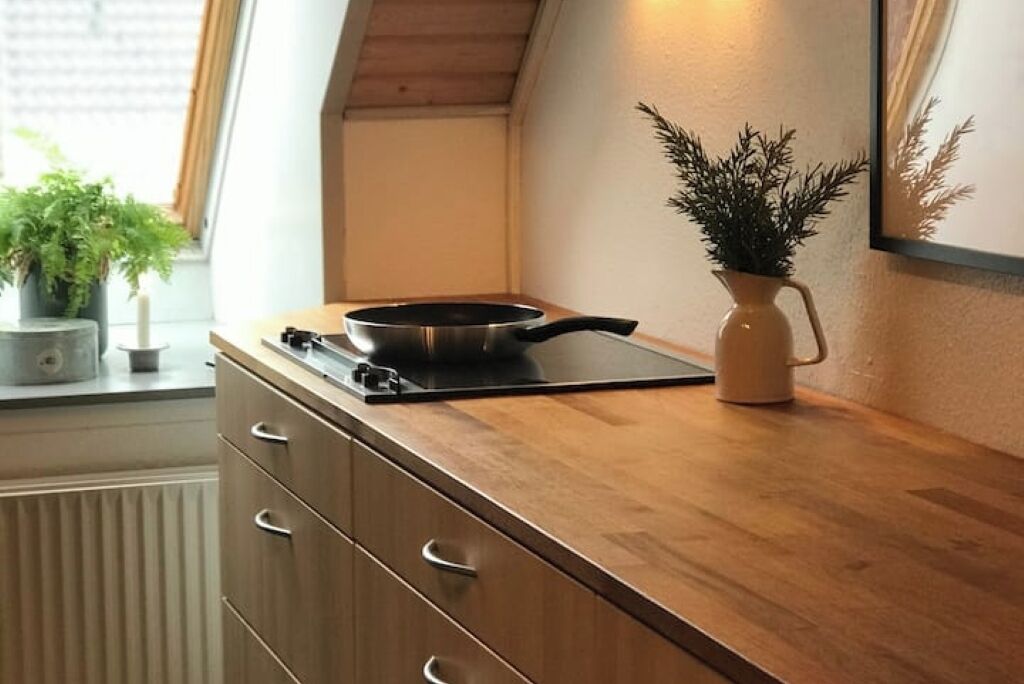 Et køkken med komfur, en potteplante og en vase på en træbordplade.