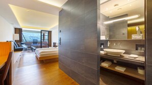 Una habitación de hotel moderna con una cama grande, un escritorio, una silla, un baño con un espejo amplio y vistas a las montañas.