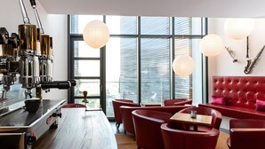 Un café moderno con una máquina de café, asientos rojos y ventanas amplias.